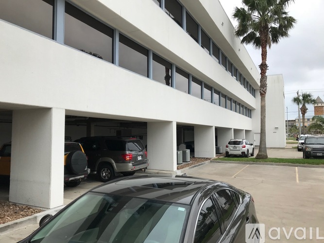 A black car is parked in a parking lot in front of a white building.