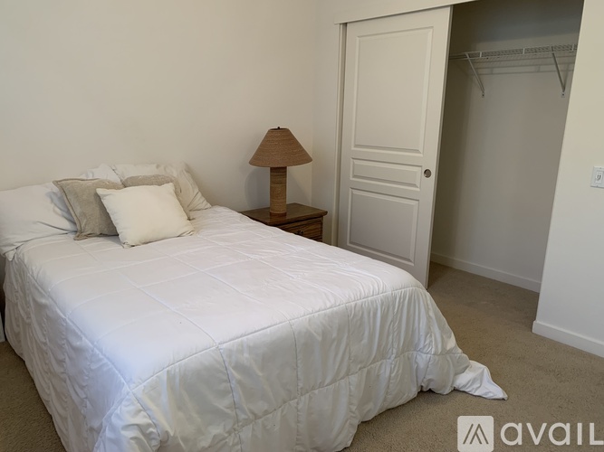 A bedroom with a white bed and a lamp on a side table.