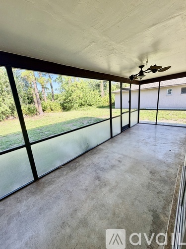 A room with a ceiling fan and large windows overlooking a grassy area.