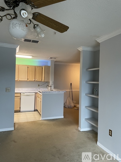 A room with a ceiling fan and a kitchen area in the background.