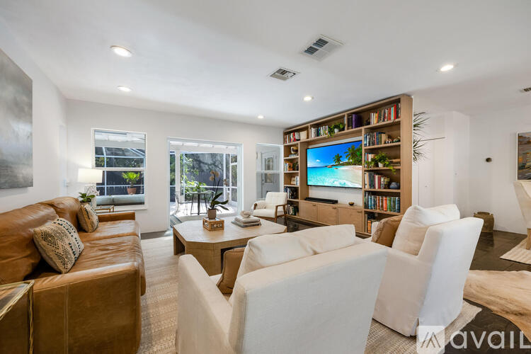 A living room with a brown leather couch, white chairs, and a bookshelf filled with books.