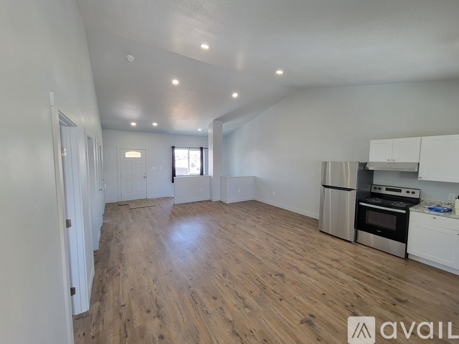 A spacious room with wooden flooring and a kitchen area with white cabinets and appliances.
