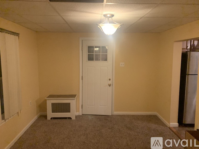 A room with a white door, a window with white curtains, and a carpeted floor.