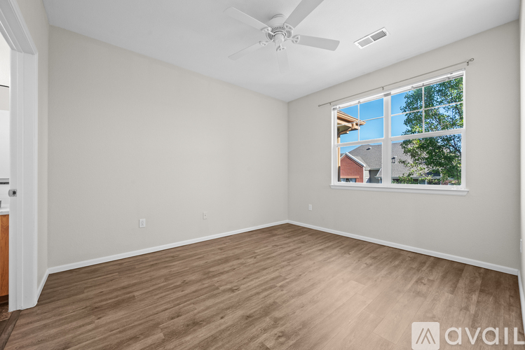 A room with a ceiling fan and a window showing a view of a house and trees.