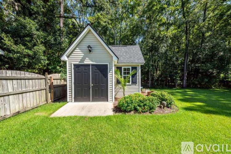 A small house with a garage door is surrounded by a well-kept lawn and trees.