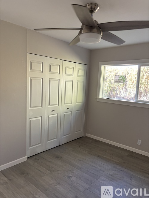 A room with a ceiling fan and a window with a view of trees outside.