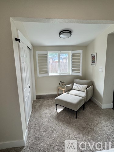 A living room with a grey sofa and a window with white shutters.