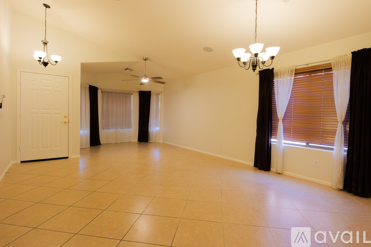 A spacious room with a white door, a chandelier, and a window with curtains.