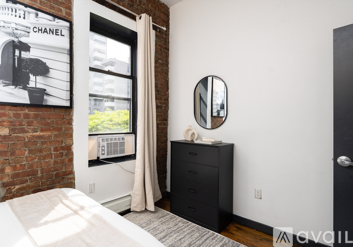A bedroom with a white bed and a black dresser with a mirror and a Chanel poster on the wall.