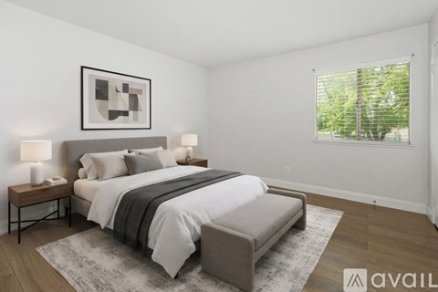 A bedroom with a large bed, a nightstand with lamps, and a framed picture on the wall.