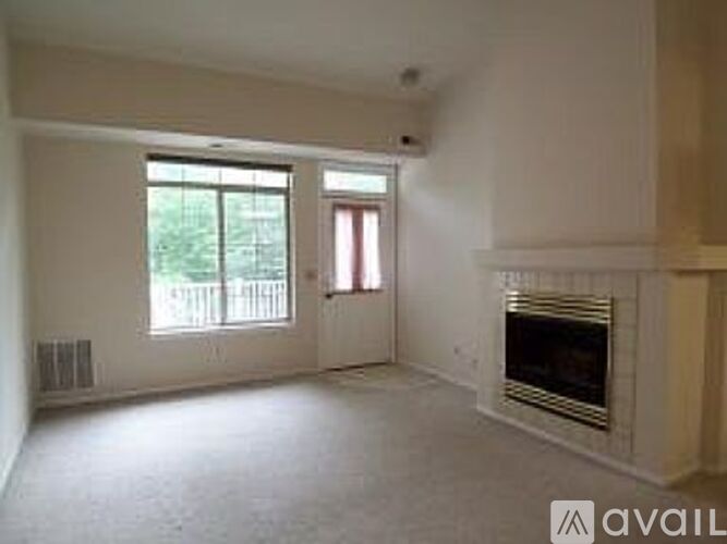 A living room with a fireplace and a window with a view of a fence.
