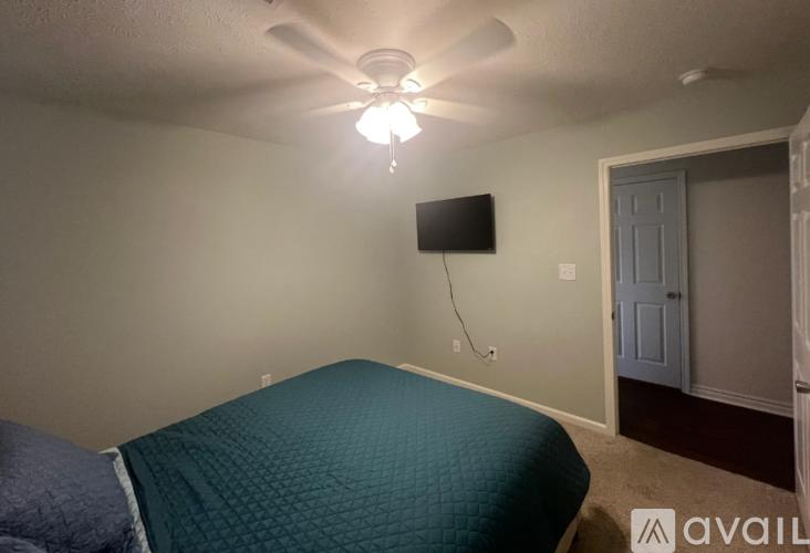 A bedroom with a bed, ceiling fan, and a flat screen TV mounted on the wall.