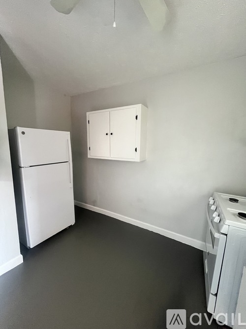 A white fridge and cupboard in a room with a white ceiling fan.