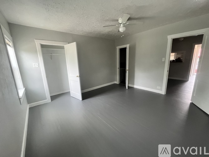 A spacious room with grey walls and floor, a ceiling fan, and three doors.