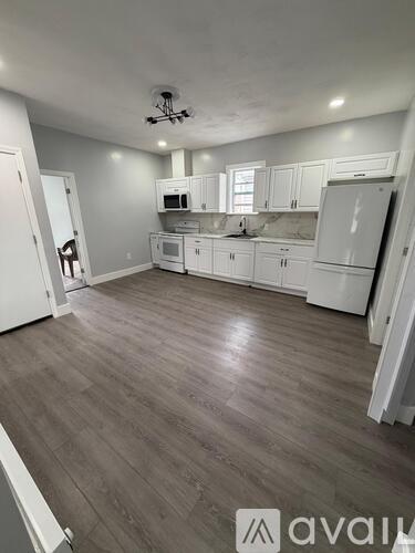 A kitchen with white cabinets and appliances, and a wooden floor.