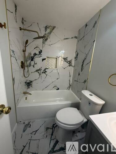 A bathroom with a marble floor and walls, a toilet, a tub, and a towel rack.