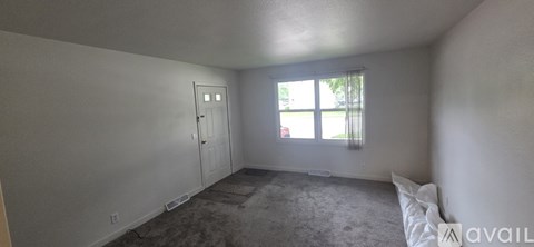 A room with a carpeted floor, a door, and a window with a view of a lawn and trees.