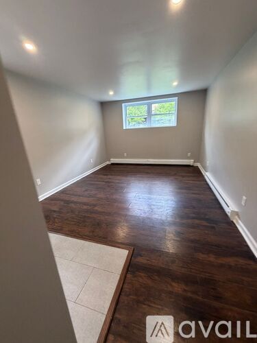 A room with wooden flooring and a window with a view of greenery outside.
