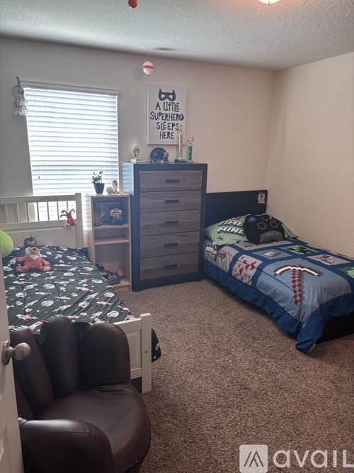 A bedroom with a bed, a chair, and a dresser with a sign that says "A little superhero sleeps here.".