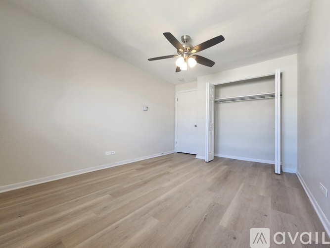 A room with a ceiling fan and light fixture, hardwood floors, and a sliding door.