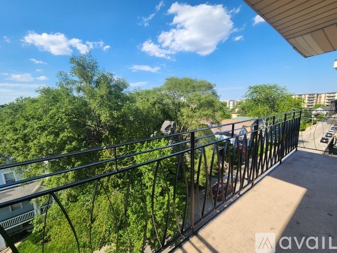 A balcony with a metal railing overlooks a green landscape and buildings.