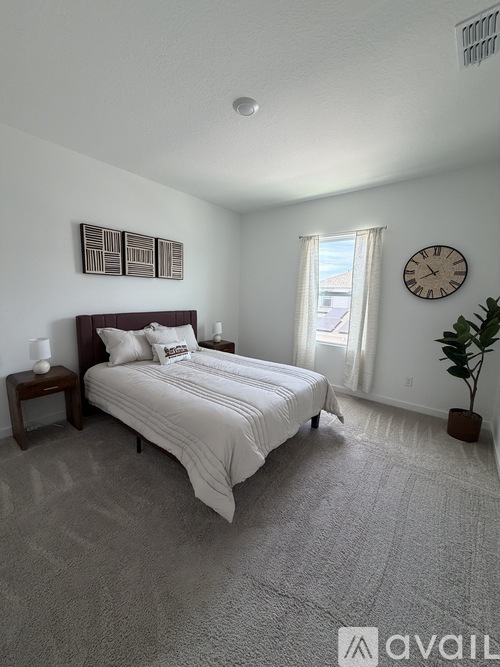 A bedroom with a large bed, a nightstand, a clock, and a plant.