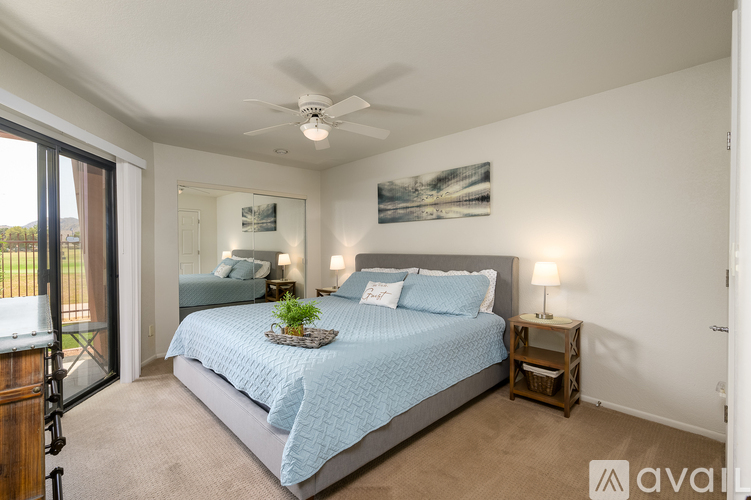 A bedroom with a bed, a ceiling fan, and a painting on the wall.