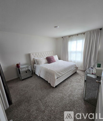 A bedroom with a large bed, nightstand, and a window with curtains.