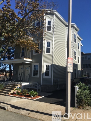 A grey house with a sign on a pole in front of it.