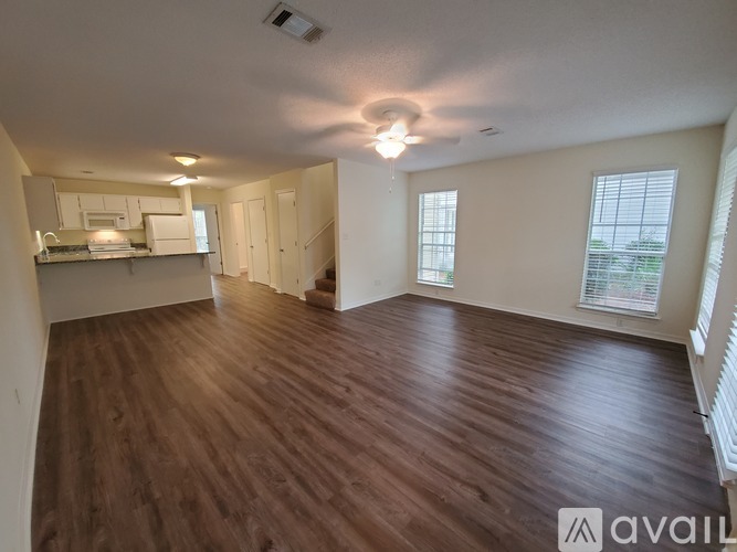 A spacious room with wooden flooring and a kitchen area in the background.
