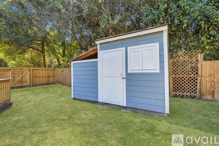 A blue shed with a white door is situated in a grassy area.