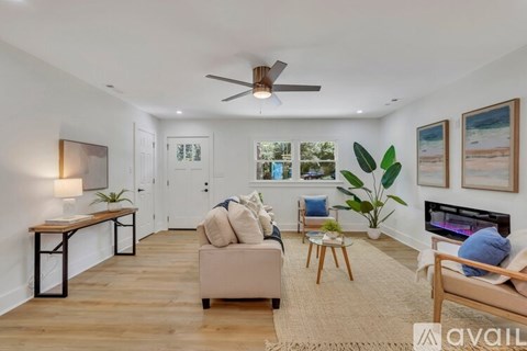 A living room with a couch, a chair, a table, a fan, and a painting on the wall.