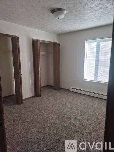 A room with carpeted floor, two open doors, and a window with blinds.