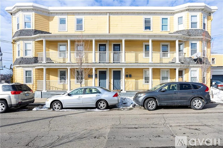 A silver car is parked in front of a yellow building.