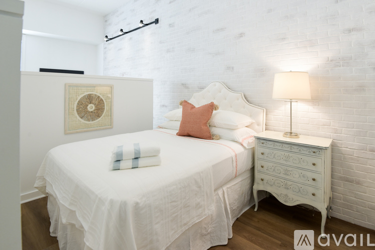 A white bedroom with a bed, nightstand, and lamp.