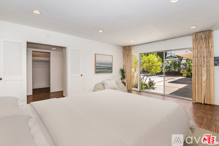 A bedroom with a large bed and a view of the backyard through the sliding glass doors.