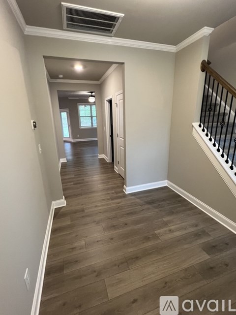 A hallway with wood flooring and a staircase with black railings.