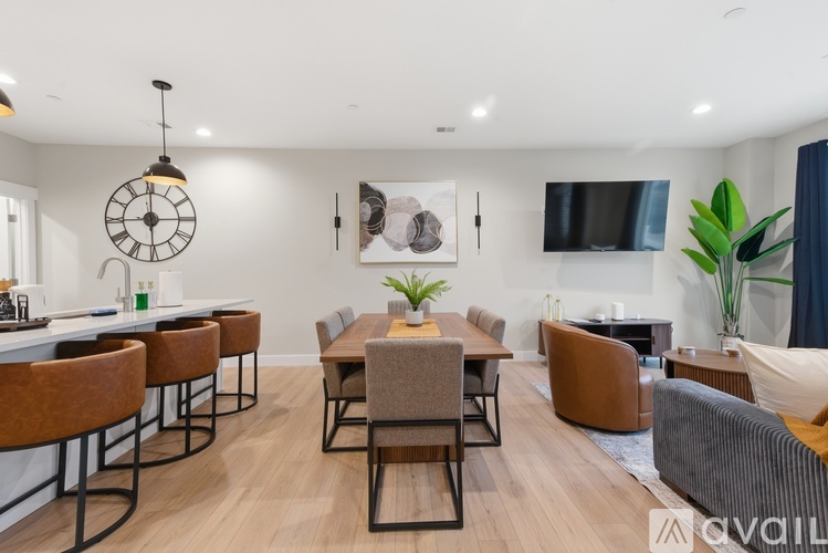 A modern living room with a large clock on the wall and a dining area with chairs and a table.