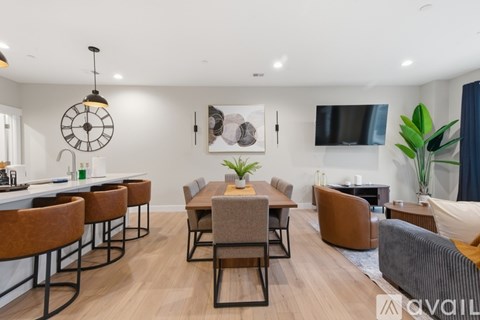 A modern living room with a large clock on the wall and a dining area with chairs and a table.