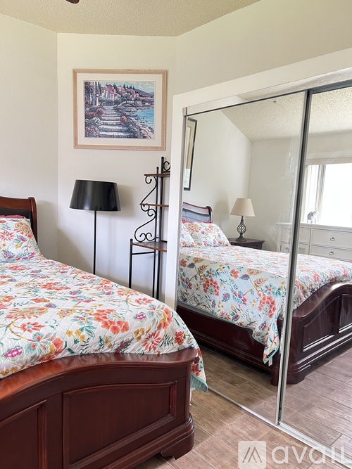 Two beds with floral bedspreads in a room with a mirror and a painting on the wall.