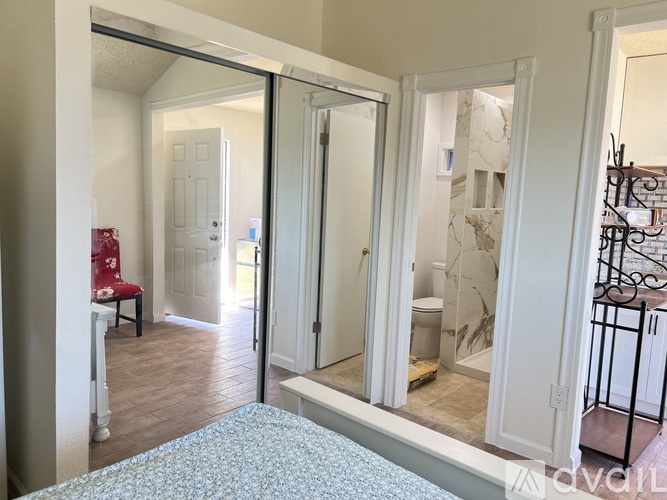 A bedroom with a bed, a chair, and a mirror.