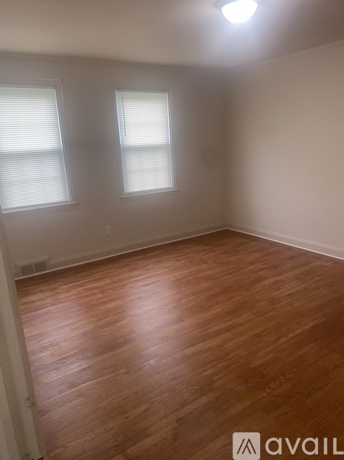 A room with wooden flooring and two windows.