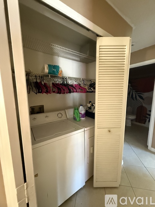 A white door is open to reveal a small laundry room with a washer and dryer.