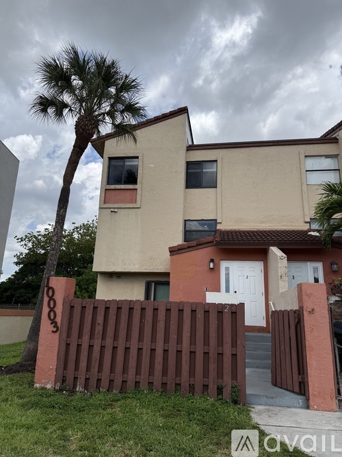 A two-story house with a brown fence and a palm tree in front.