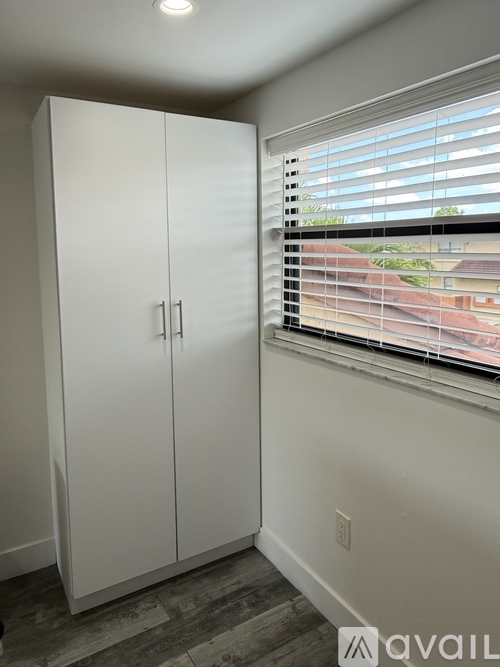 A white double door cabinet in a room with a window covered by blinds.