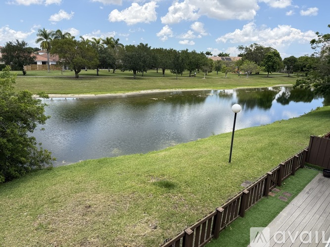 A serene park with a pond, trees, and a wooden fence.