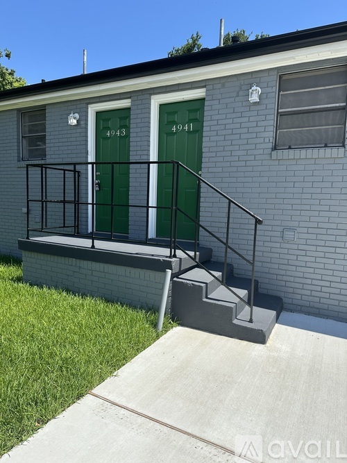 A grey building with green doors and a black railing on the steps.