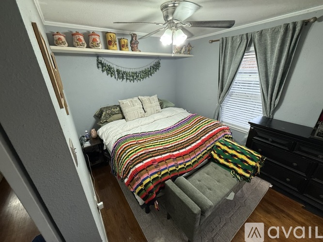 A bedroom with a bed covered in a multicolored blanket and a ceiling fan above.