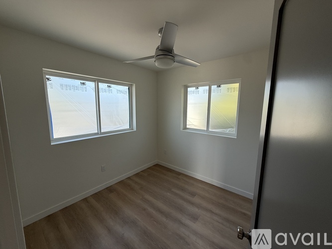 A room with a ceiling fan and two windows.