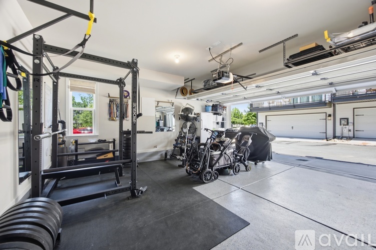 A gym with a weightlifting rack, a rowing machine, and a baby stroller.